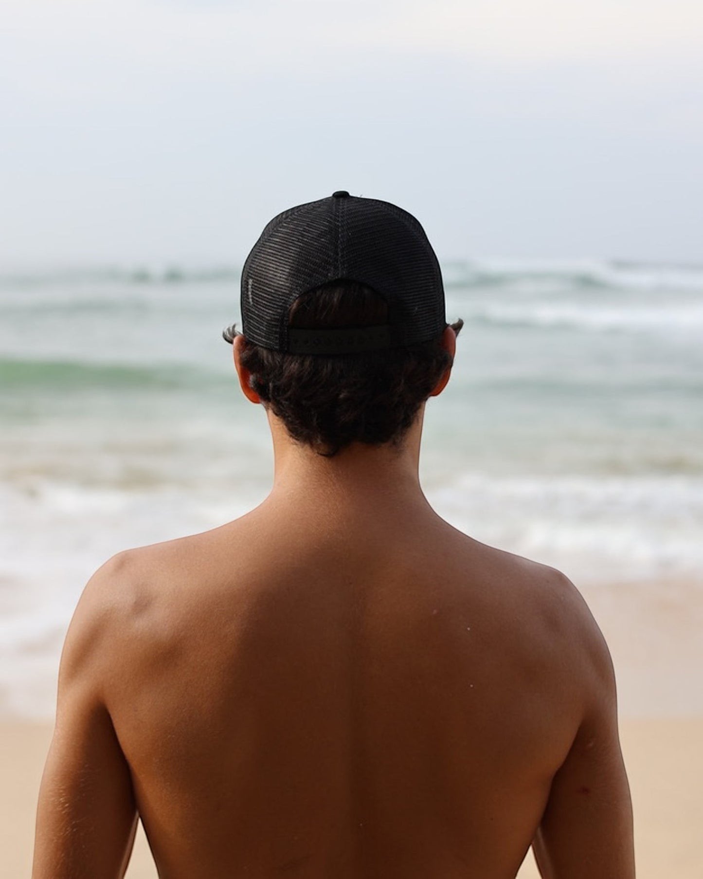 Hang Ten black trucker cap with mesh back and adjustable snapback closure, featuring a front logo patch.