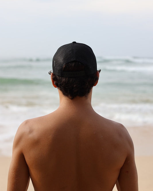 Hang Ten black trucker cap with mesh back and adjustable snapback closure, featuring a front logo patch.